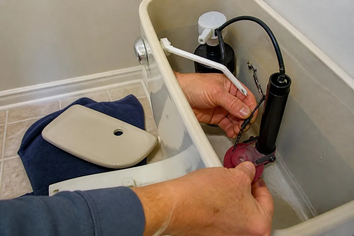 Hands replacing a flapper and fill valve in a toilet tank, toilet repair in Atlanta, GA